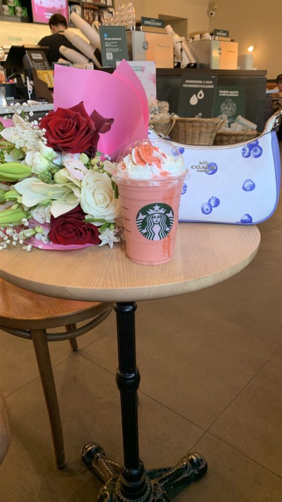 Bouquet of red and white roses next to a pink Starbucks drink and a blue handbag on a café table